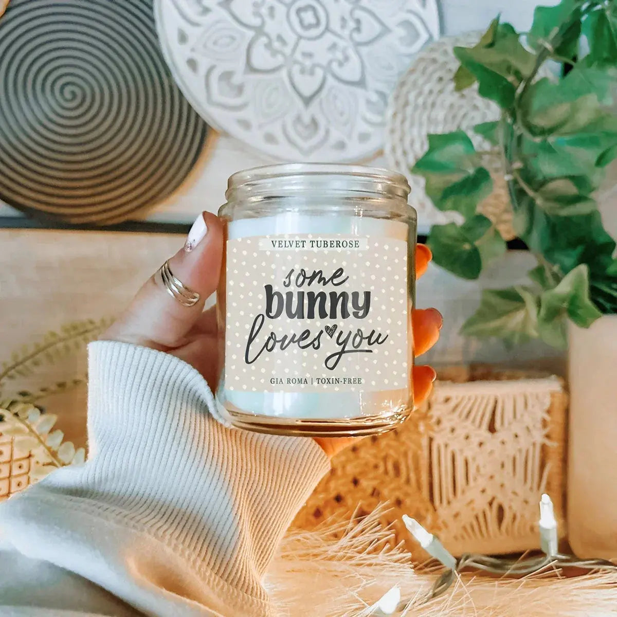 Hand holding a candle jar with 'some bunny loves you' text in a home setting.