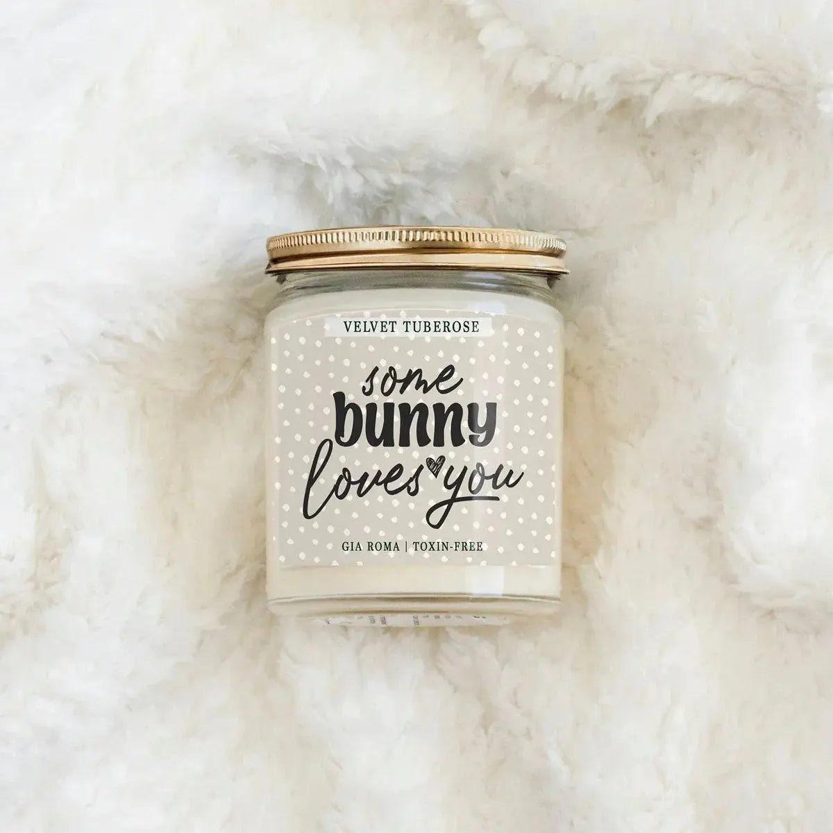 Candle jar with 'some bunny loves you' text on a fluffy white surface