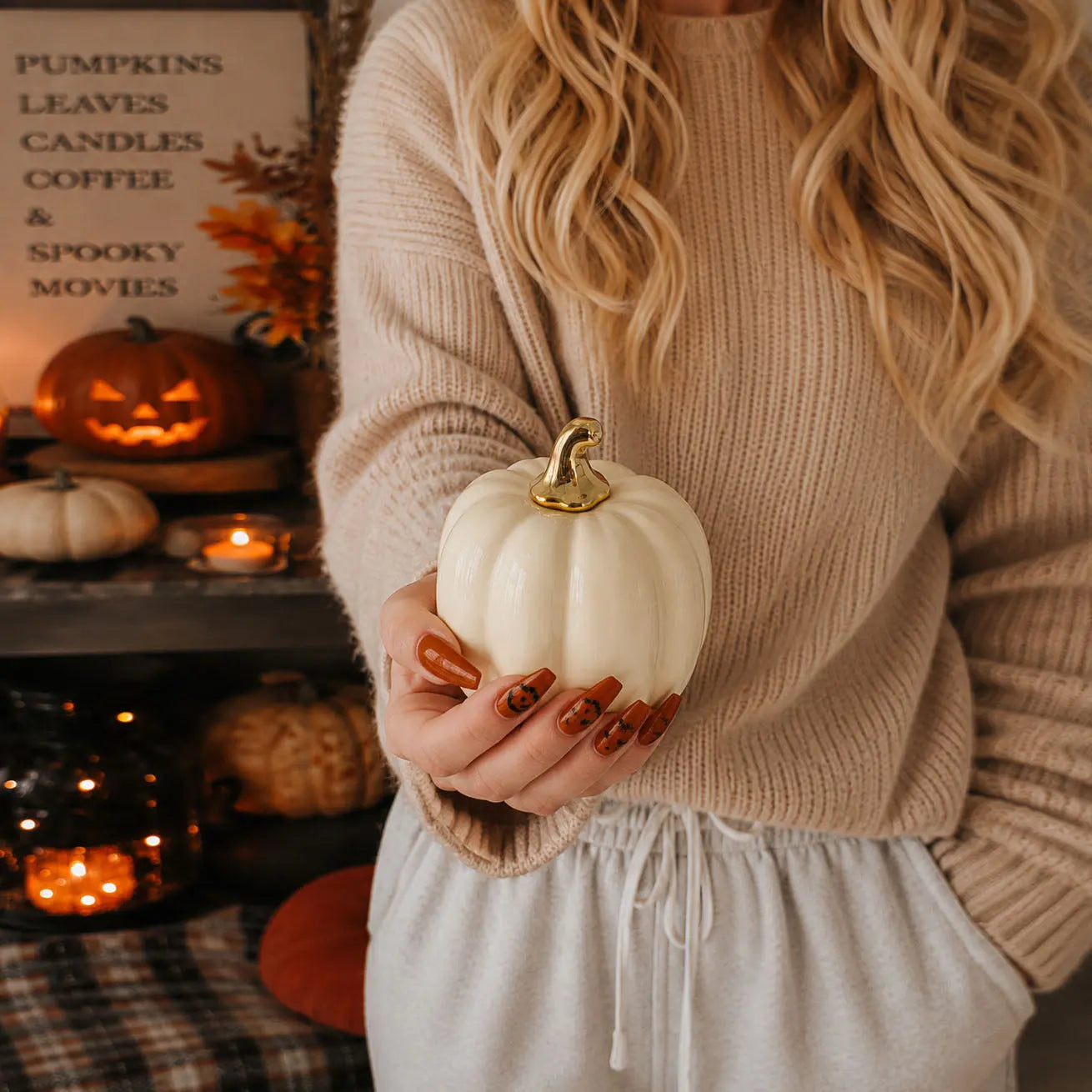 Person holding a white pumpkin with a gold top in a cozy indoor setting with Halloween decorations.