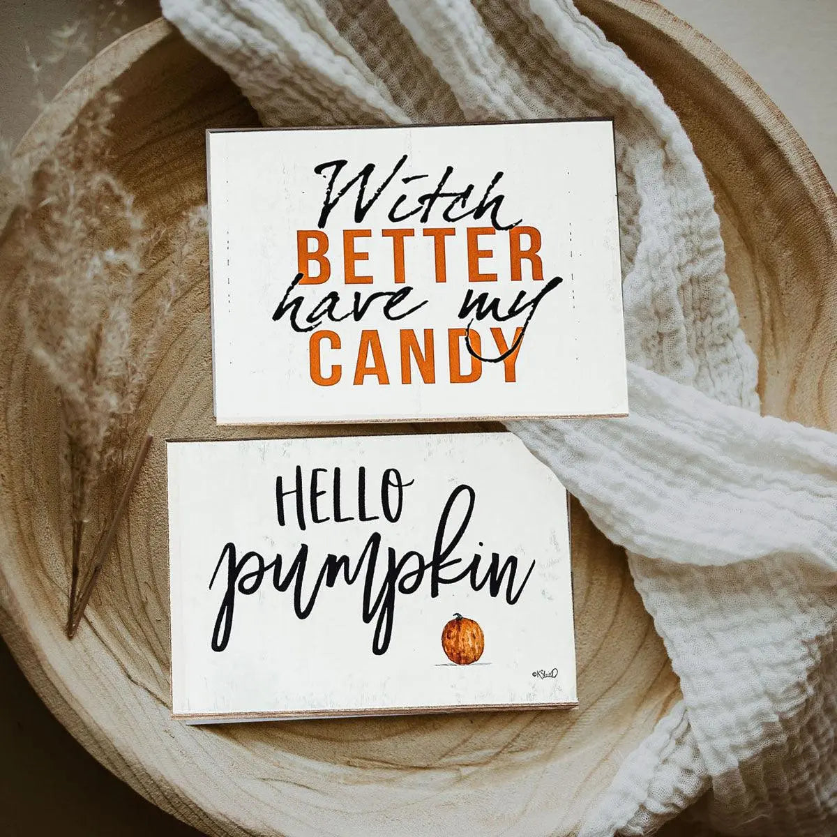 Two Halloween-themed signs on a wooden surface with a white cloth.