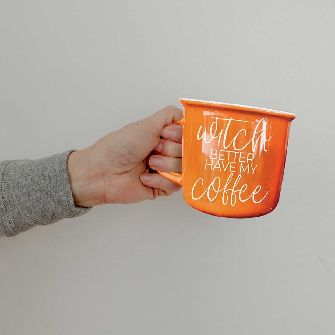 Hand holding an orange mug with text against a plain background