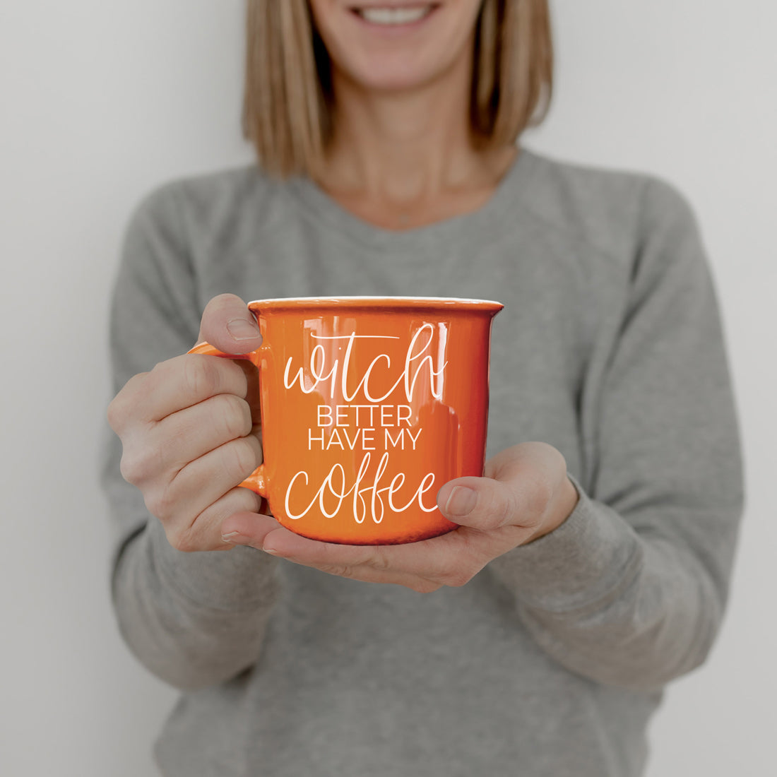 Person holding an orange mug with text against a plain background