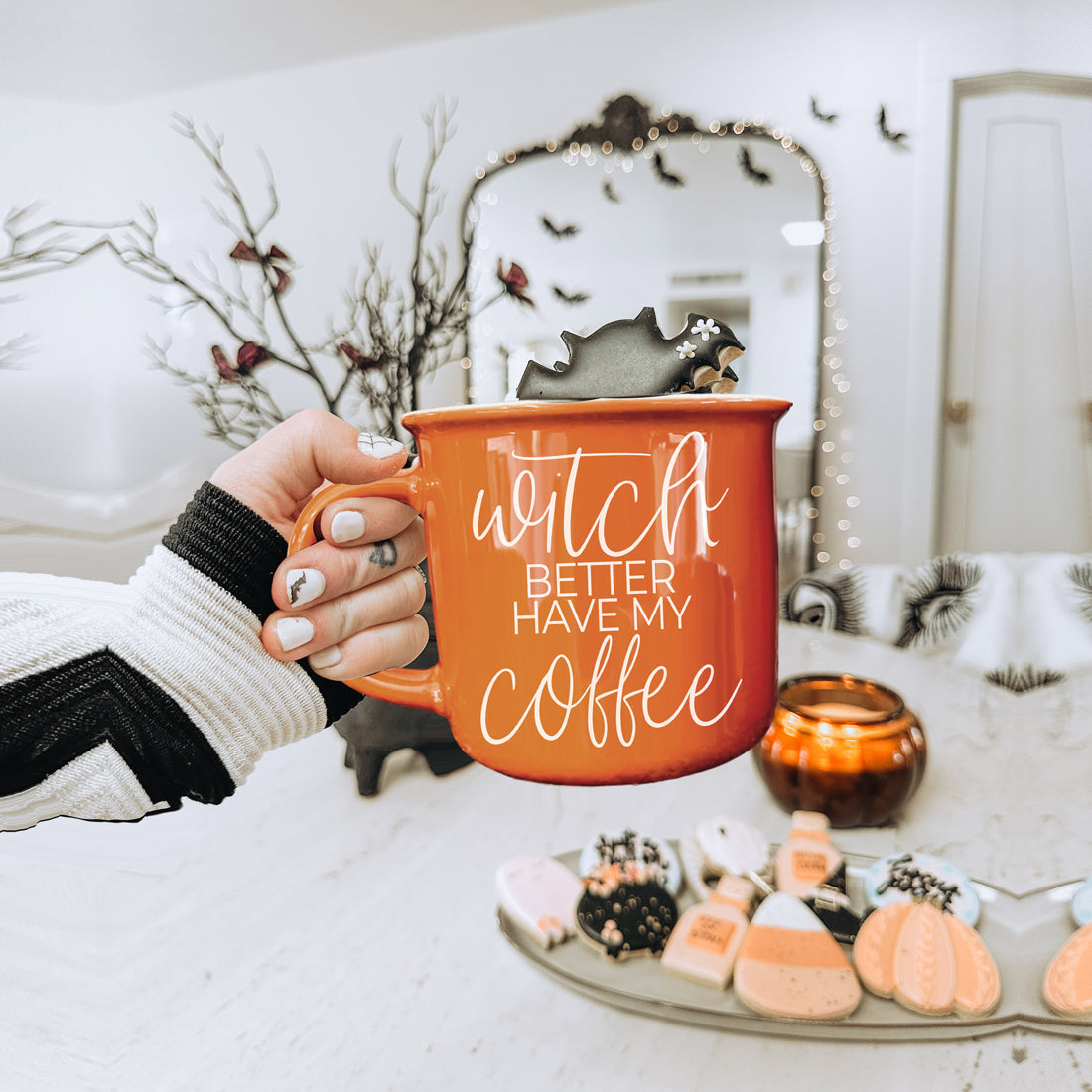 Person holding an orange mug with 'Witch better have my coffee' text, surrounded by Halloween-themed decor.