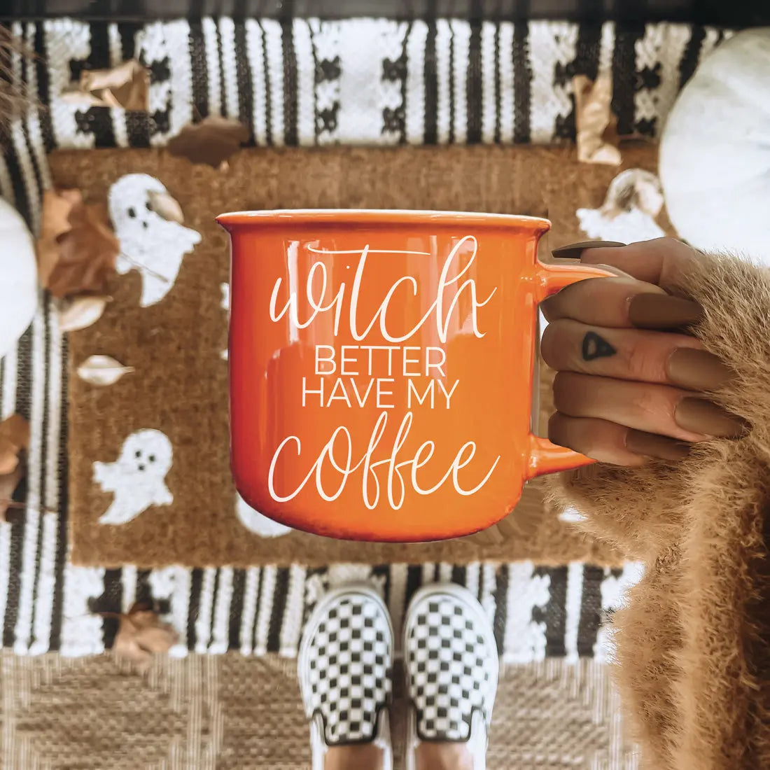 Person holding an orange mug with text, sitting on a patterned chair.