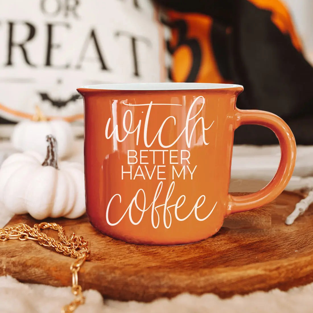 Orange mug with 'Witch better have my coffee' text on a wooden surface with pumpkins and a blurred background.