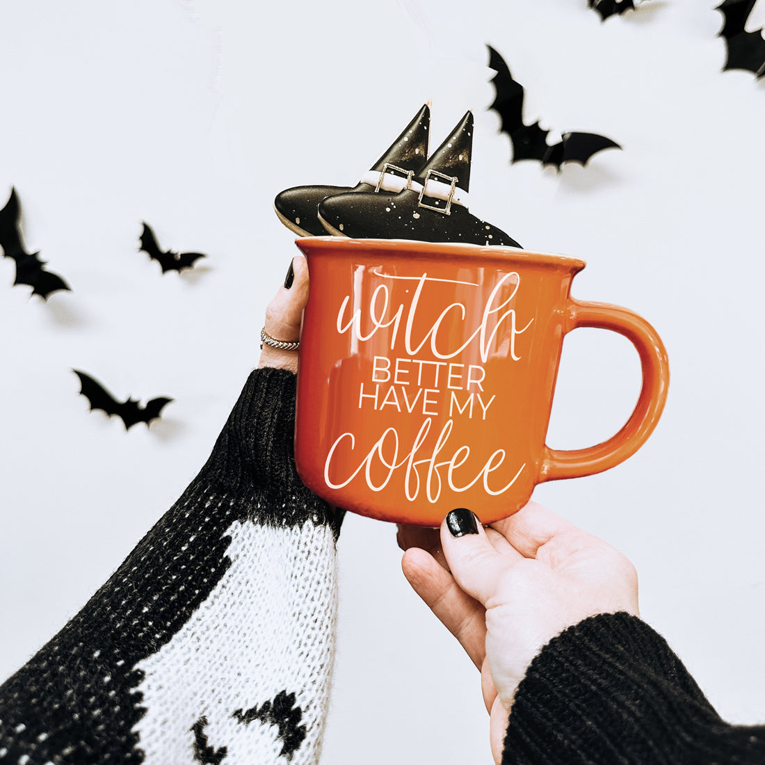 Person holding an orange mug with 'Witch better have my coffee' text, surrounded by Halloween decorations.