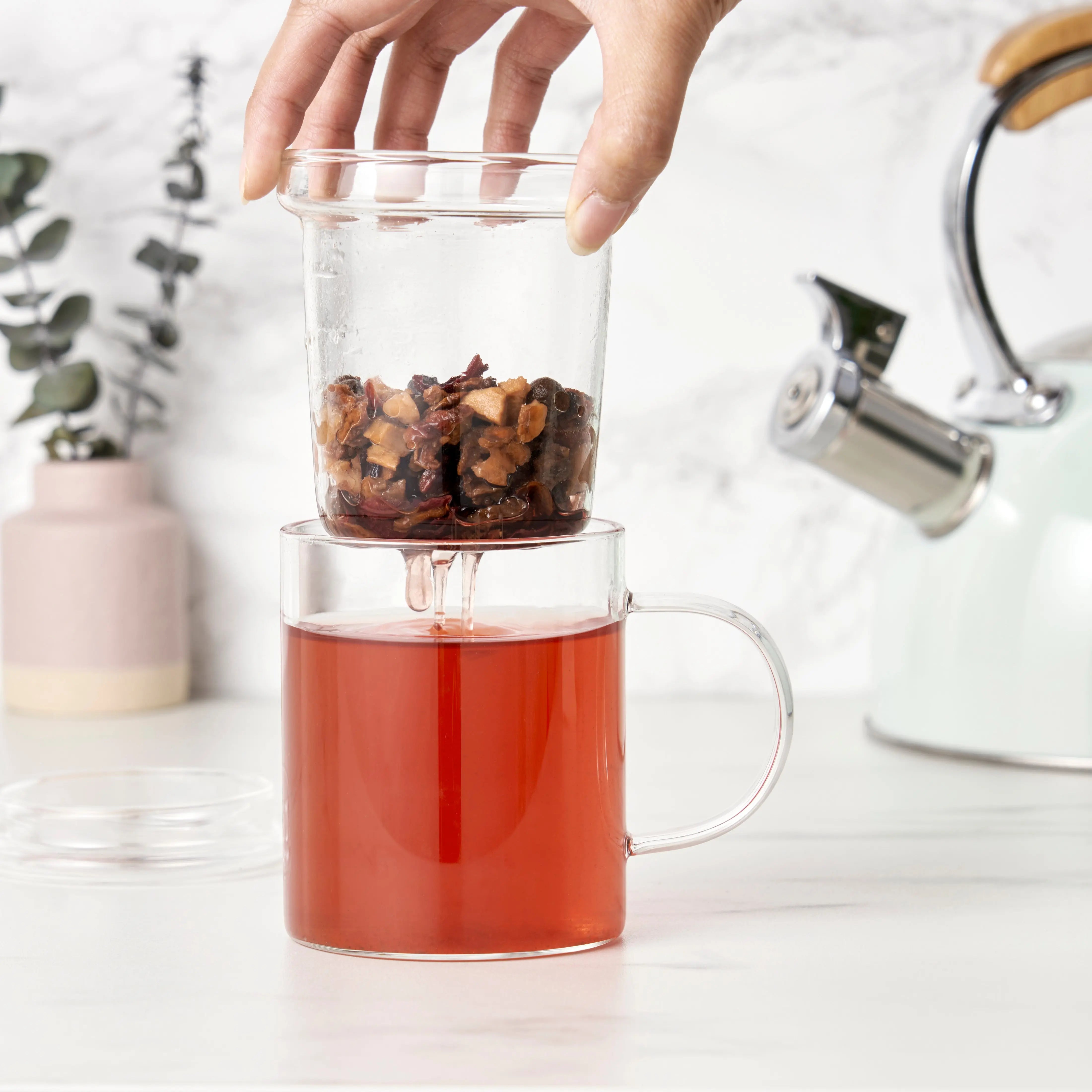 Glass mug with tea and tea leaves, hand reaching in, white background